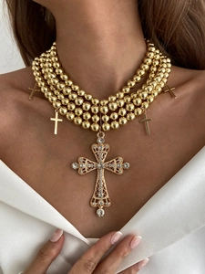 Détail macro d'un collier multirangs doré avec un grand pendentif croix serti de cristaux