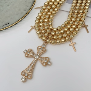 Détail d'un collier à trois rangs de perles dorées avec pendentifs croix en strass