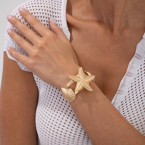 Detail of gold starfish and shell open cuff bracelet worn on a female wrist