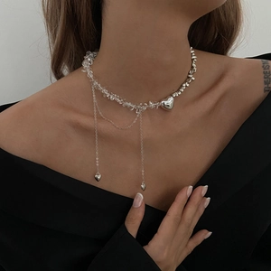 Dettaglio della collana con pendente a cuore asimmetrico, perle trasparenti e nappe