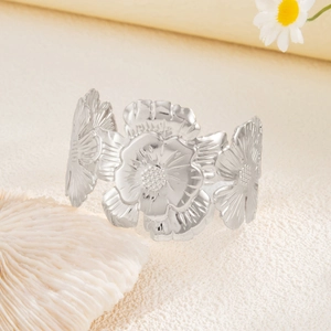 Macro detail of wide silver cuff bracelet featuring intricate carved metallic floral petals