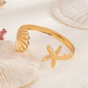 Close-up of gold starfish and seashell details on an open cuff bracelet over white sand
