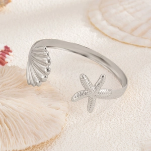 Detail of silver starfish and seashell open bracelet on white sand with ocean props