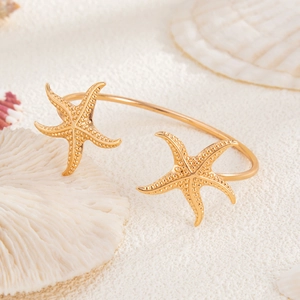 Close-up of gold starfish open cuff bracelet with sea corals and shells background