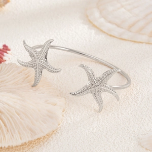 Detail of silver starfish bangle featuring textured surface on a sandy beach setting