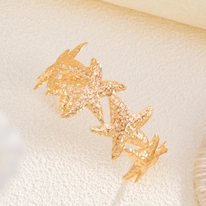 Detail of five linked gold starfish with hammered metal texture on sandy surface