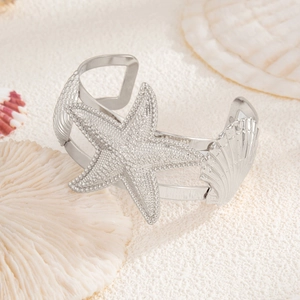 Silver ocean style starfish and shell cuff bracelet on white sand beach background