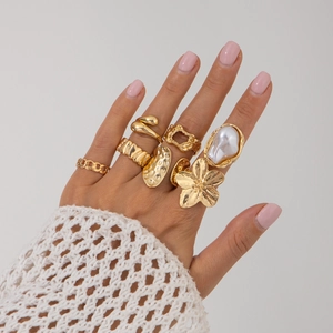 Detail van gouden stapelbare ringen met barokke parels, bloemaccenten en kettingtexturen