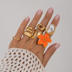 Detailoverzicht van zeven vergulde ringen met barokparel en oranje bloemmotief
