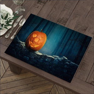 Macro shot of Halloween linen placemat with glowing pumpkin on dark wooden dining table