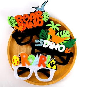 Detailed view of three dinosaur felt party glasses with ROAR text on wooden tray