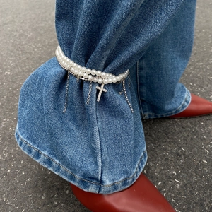 Zweireihiges Perlen-Fußkettchen mit Strass-Kreuz-Anhänger über blauen Jeanshosen