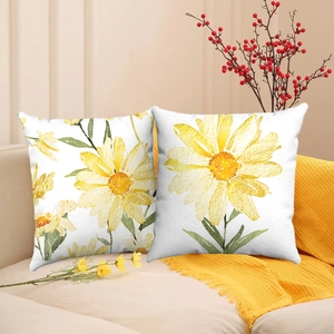 Set of two white linen cushion covers with yellow daisy print on a cozy sofa