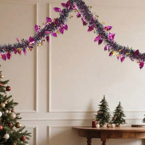 Dark green Christmas tinsel garland with purple leaves and gold sequins on a white wall