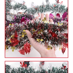 Close-up of dark green Christmas tinsel garland with red holly leaves and white trim