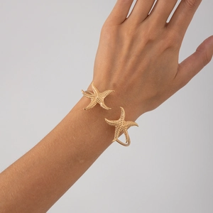 Detailaufnahme eines goldenen Seestern-Armreifs mit strukturierter Oberfläche am Gelenk