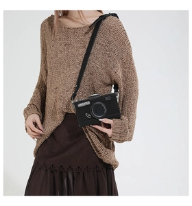 Detail of creative vintage camera crossbody bag worn over a brown knit sweater