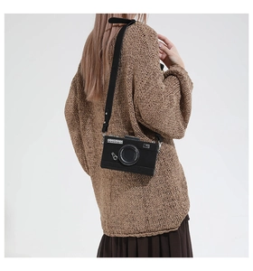 Detail view of a vintage camera-shaped crossbody bag on a beige sweater outfit