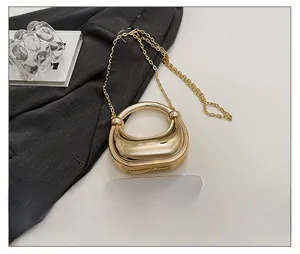 Close-up of gold mirror finish crescent bag with metal handle and chain against a phone