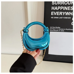 Detail of blue metallic half-moon mini bag with gold chain and round handle grip