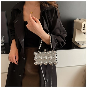 Detail of silver metallic mirror bag with spherical studs held by model in black trench coat