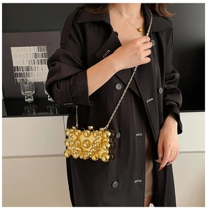Detail of gold chain bag with spherical textures and metal strap on black trench coat