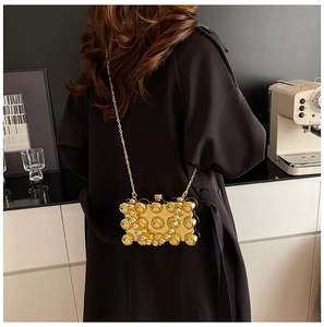 Detail of gold studded clutch bag with acrylic chain worn by a model in luxury setting