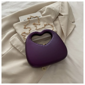 Detail of deep purple heart-shaped acrylic evening bag with gold chain on beige blazer