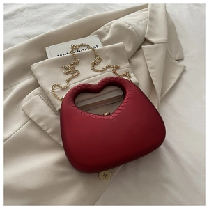 Deep red heart-shaped hard shell clutch with gold chain strap on white fabric