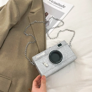Detail view of silver camera-shaped crossbody bag with scale texture and metal chain strap