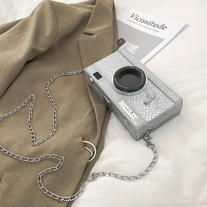 Detail of silver embossed camera-shaped crossbody bag with chain strap and quote
