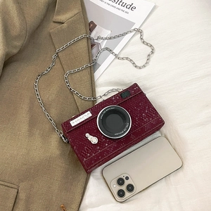 Camera-shaped shoulder bag in burgundy snakeskin leather shown next to a smartphone