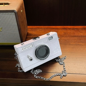 Macro detail of white camera-shaped handbag with crocodile texture and silver chain strap