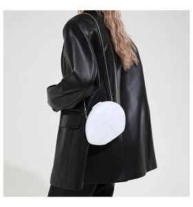 Modell mit weißer Abendtasche in Marmor-Optik mit goldener Kette über einem schwarzen Blazer