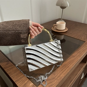 Detalle de bolso plateado ondulado con asa dorada y correa de cadena de metal