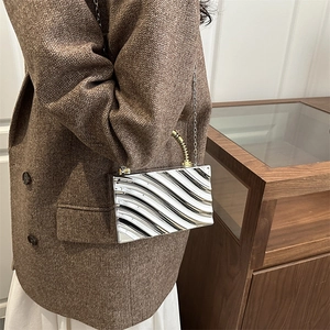 Bolso de mano rígido plateado ondulado con asa dorada y cadena de hombro en modelo