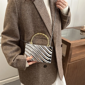 Detalle de bolso rígido plateado con textura ondulada y asa de cuentas doradas en modelo