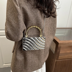 Detalle de bolso bandolera plateado con textura ondulada y asa de bambú dorada en chaqueta