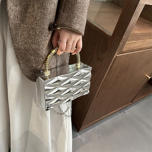 Bolso de mano plateado geométrico con asa de bambú y cadena metálica en mano
