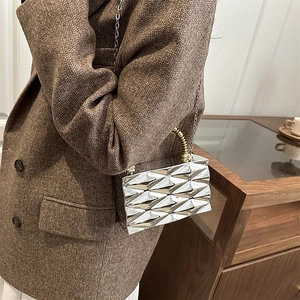 Detalle de bolso geométrico plateado con asa en espiral dorada sobre blazer marrón