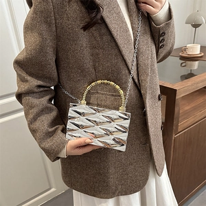 Detalle de bolso acolchado plateado con asa de cuentas doradas y correa de cadena