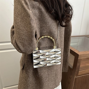Detalle de bolso bandolera plateado geométrico con textura metálica y asa de cuentas doradas