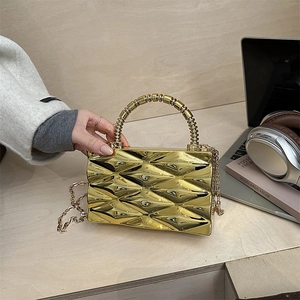 Detalle de un bolso caja metálico dorado con textura geométrica y correa de cadena