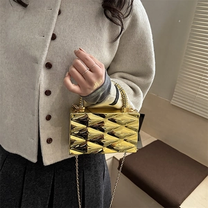 Detalle de un bolso de fiesta dorado con textura geométrica y asa metálica en espiral