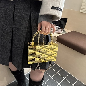 Detalle de bolso caja metálico dorado con diseño acolchado y asa de cuentas