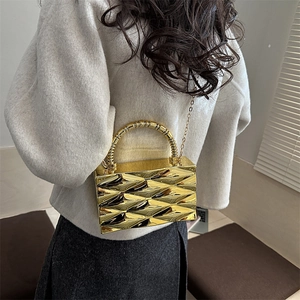 Detalle de bolso clutch metálico dorado con textura geométrica 3D y asa de cadena