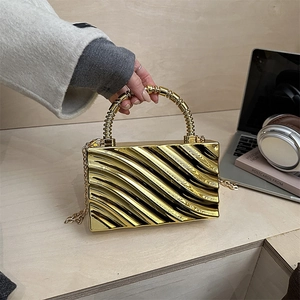 Primer plano de bolso clutch dorado con textura de ondas y asa de cuentas a la moda