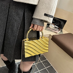 Detalle de un bolso de mano dorado metálico con texturas onduladas y asa espiral elegante