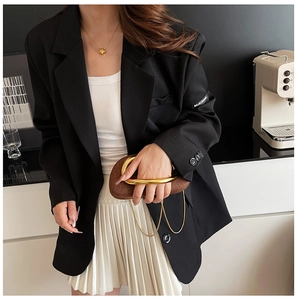 Detail view of a brown woven clutch bag with a metallic circular handle in a lifestyle setting