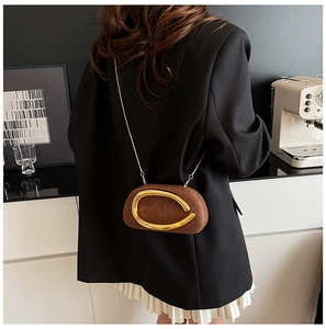 Brown woven crossbody bag with gold horseshoe buckle and chain shown on model